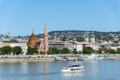 Boats in river by buildings in city against sky