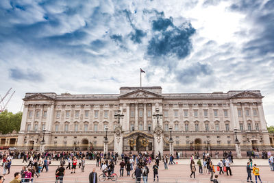 People walking on street by government building against cloudy sky