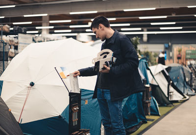 A young man reads the instructions for a tent in a store.