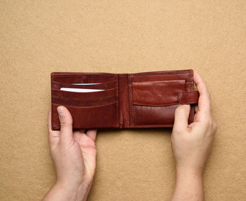 Cropped image of hand holding wallet against brown background