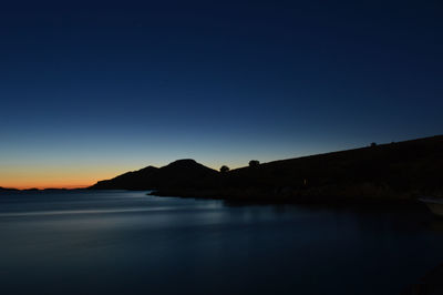 Scenic view of silhouette mountains by lake against sky at sunset