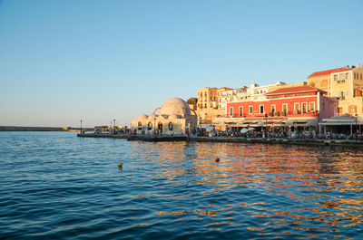 Buildings by sea against clear blue sky