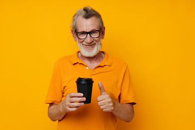 Portrait of senior man holding cup gesturing against yellow background