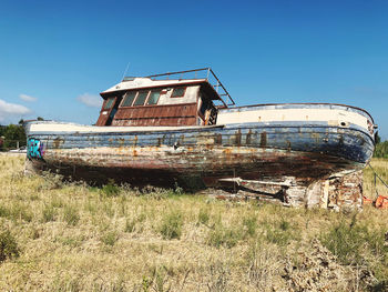 Abandoned boat on field against clear blue sky