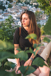 Beautiful woman sitting on bench by plants