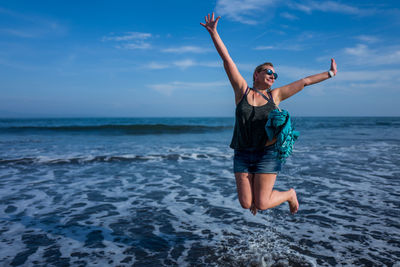 Full length of mature woman jumping on shore at beach against sky