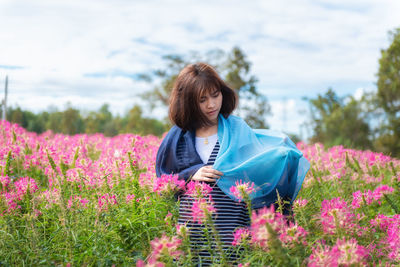 Woman with scarf standing by blooming flowers against sky