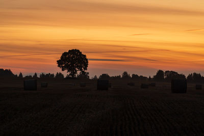 Silhouette hay bales on field against sky during sunset
