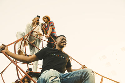 Low angle view of young man sitting against sky