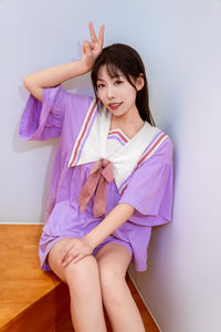 A smiling girl in a purple outfit poses on the stairs with a peace sign