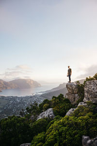 Male hiker standing on cliff against sky during sunset