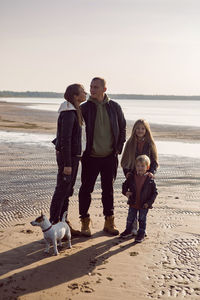 Family in a leather jacket stands along the beach with their dog in autumn