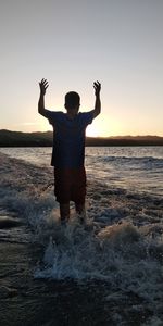 Rear view of man standing at beach during sunset