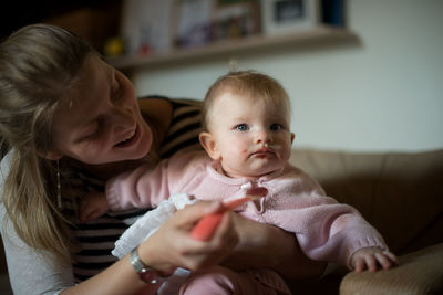 Portrait of happy mother holding baby sitting at home