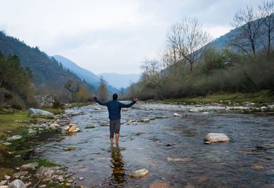 Rear view of man standing on rock against sky