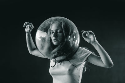 Young woman wearing glass container against black background