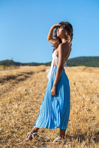 Woman with arms raised standing on field against clear blue sky