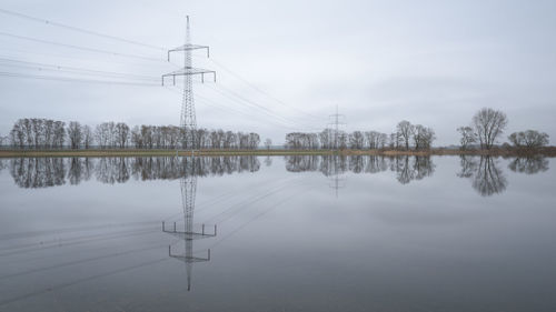 Electricity pylons by lake against sky