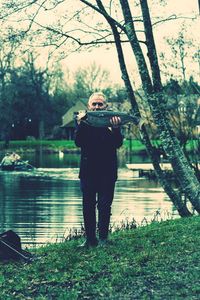 Portrait of mature man holding fish while standing by lake