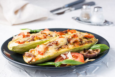 Ready-to-eat baked zucchini halves filled with cheese and tomato and basil leaves on a black plate 