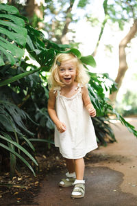 Portrait of happy little girl kid standing against plants