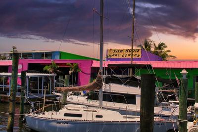 Sailboats moored at harbor against sky during sunset