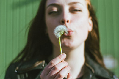 Close-up portrait of young woman blowing dandelion