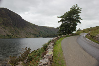 Scenic view of road by tree mountains against sky