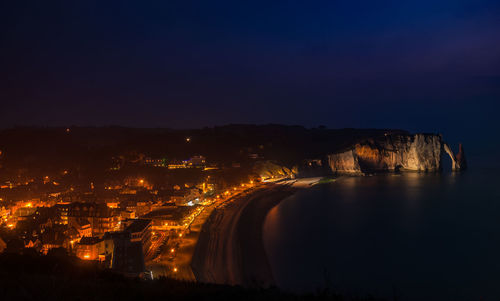 High angle view of illuminated cityscape by sea against sky at night