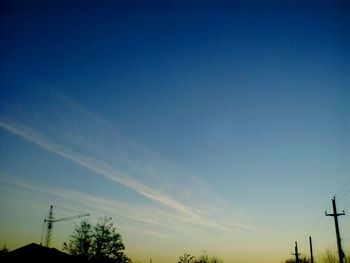 Low angle view of silhouette vapor trail against blue sky