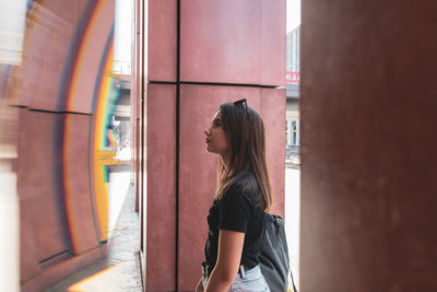 Side view of young woman standing by columns