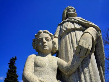 Low angle view of old statue of jesus and child against blue sky.