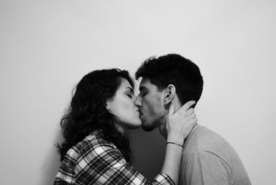 Side view of young couple kissing against white background