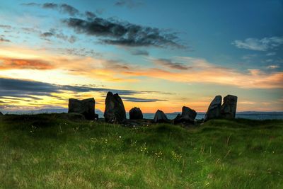 Rocks on grassy field against sky at sunrise