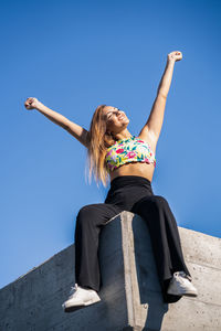 Low angle view of woman sitting against blue sky