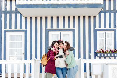 Happy women friends using mobile phone in front of colorful houses.costa nova, aveiro, portugal