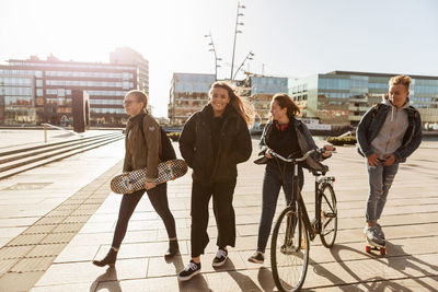 Teenage friends walking with bicycle and skateboards on pedestrian zone in city