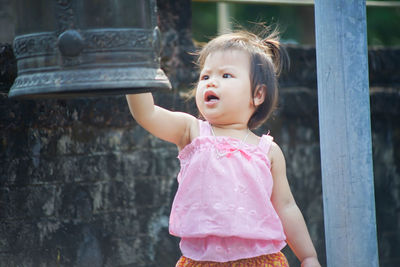 Cute baby girl looking at bell while standing outdoors