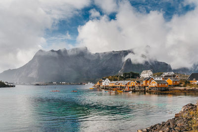 Houses on rock formation by river against cloudy sky