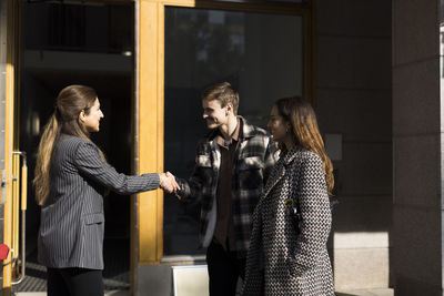 Happy couple shaking hand with female real estate agent in front of apartment