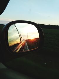 Close-up of side-view mirror against sunset sky