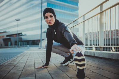 Full length of beautiful woman wearing hijab exercising against building during sunrise