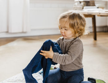 Cute baby girl holding jeans while sitting on floor at home