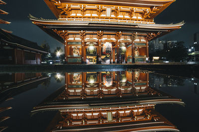 Reflection of illuminated shrine on reflecting pool at night