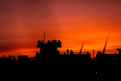 Silhouette cranes against orange sky during sunset