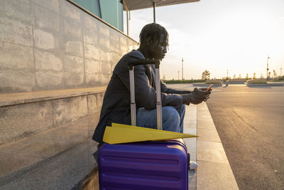 Businessman using smart phone with suitcase and paper airplane on steps