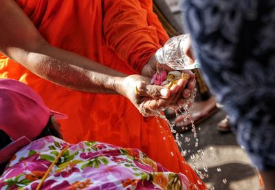 Cropped image of person pouring water for monk