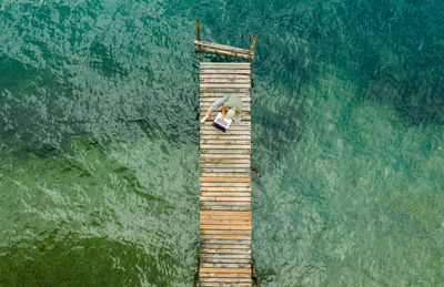 Aerial view of man using laptop sitting on pier in sea