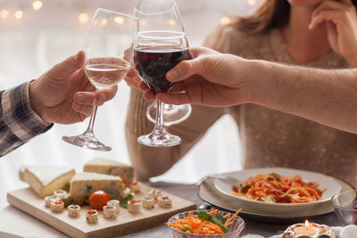 Close up of unrecognizable friends toasting with wine during lunch at dining table.