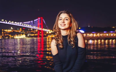 Portrait of smiling young woman standing in river at night